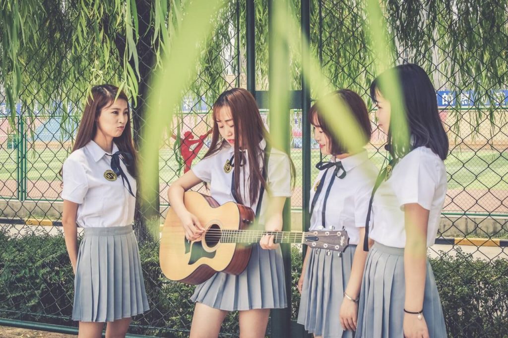 Asian schoolgirl with a guitar surrounded by other schoolgirls